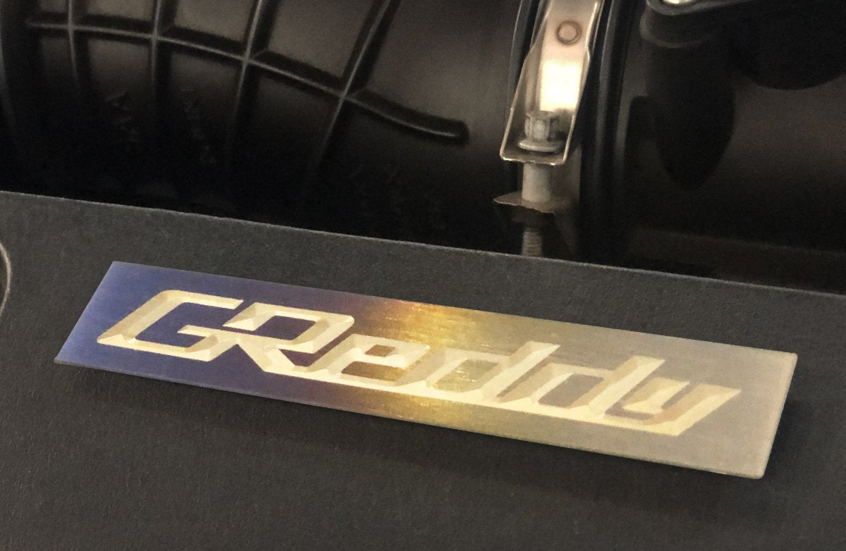 GReddy Optional Titanium GReddy Emblem - (105x20mm)